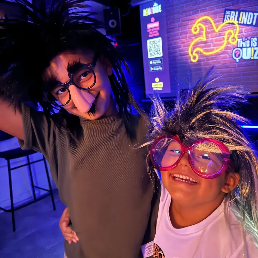 Enfants déguisés avec perruques et lunettes rigolotes pendant un anniversaire karaoké et blind test à Black Holes Minigolf, Chambly